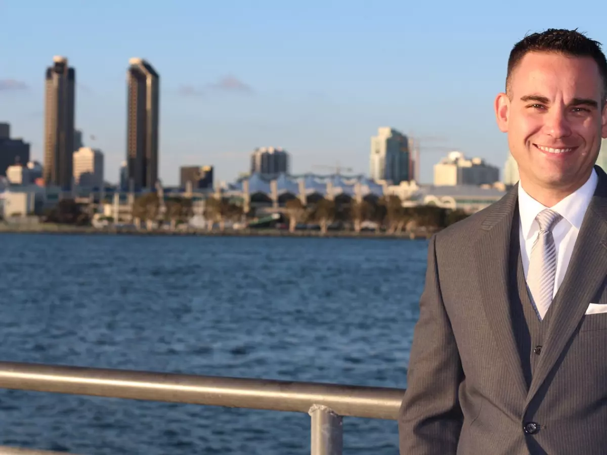 A man in a suit is standing in front of a cityscape.